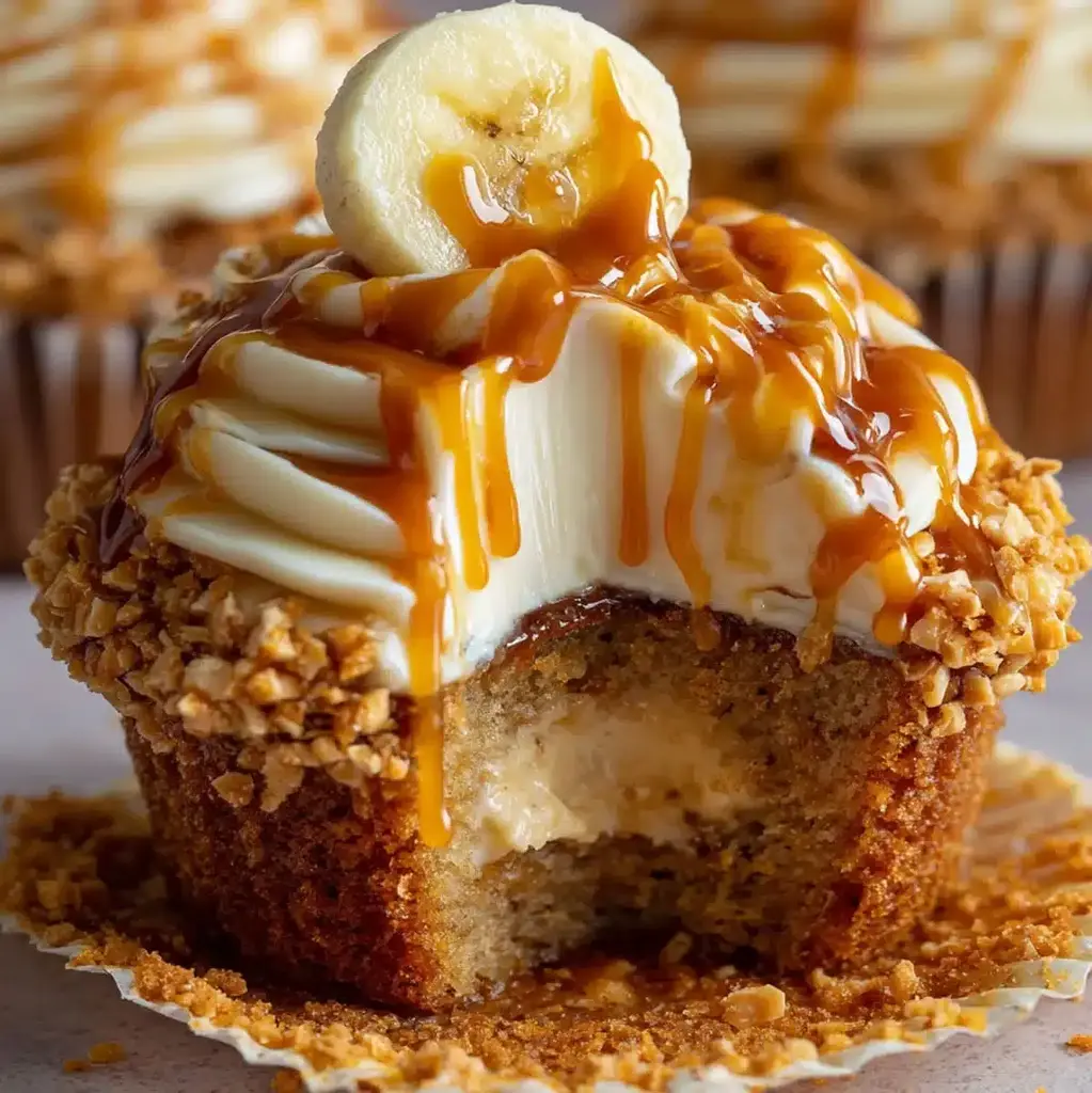 Delicious banana cheesecake cupcakes topped with cream cheese frosting, peanuts, and caramel drizzle.